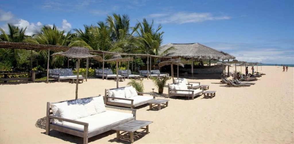 Lounge de praia exclusivo do UXUA Hotel em Trancoso, com sofás brancos na areia, ideal para um dia de sol a dois.